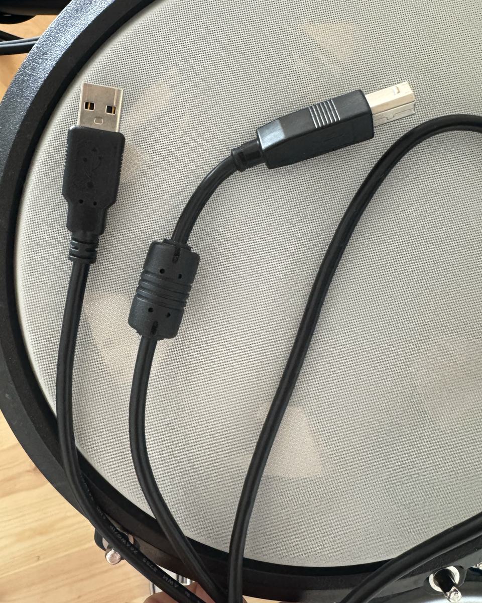 A black USB cable with a flat USB-A plug at one end and a square USB-B plug at the other.