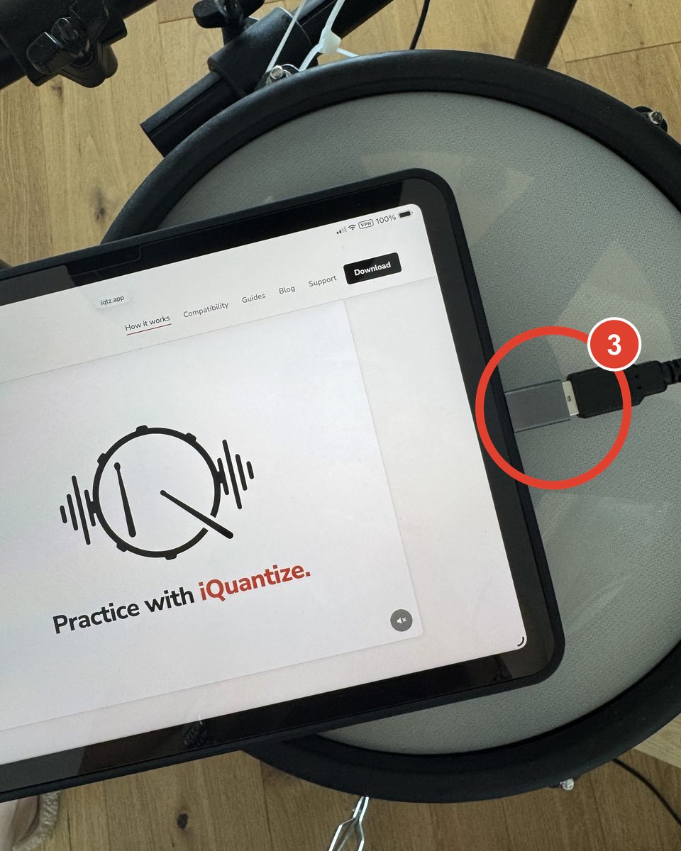 An iPad with a USB-C port on a drum pad, the grey adapter in its USB-C port and the kit cable connected.