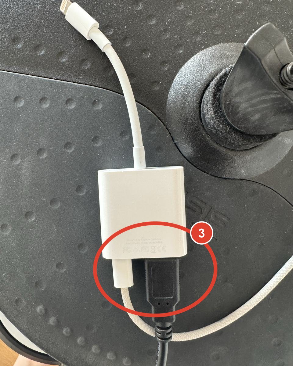 The camera adapter with the black kit cable in its USB port and a white charging cable in its Lightning port.